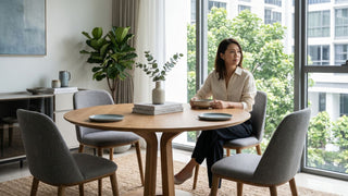 Woman seated at a round wood dining table with grey chairs in a bright Singapore condo dining area.