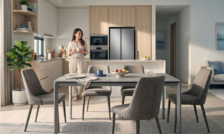 Woman standing in a bright Singapore open-plan kitchen with a Samsung fridge beside a modern dining table.