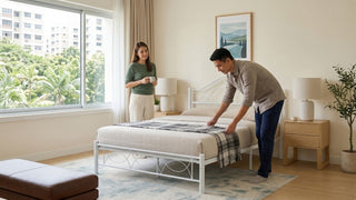 Singaporean couple arranging bedding on a white metal bed frame with mattress