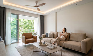 Woman relaxing on a beige sofa in a Singapore living room with a ceiling fan, recessed lighting and balcony windows.