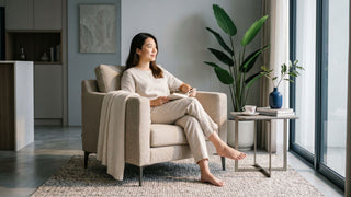 Woman relaxing with a book on a beige single sofa chair beside a window in a modern Singapore home.