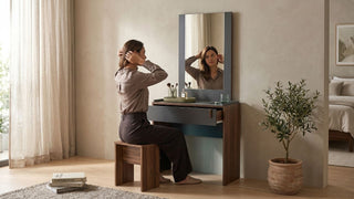 Woman sitting at a small dressing table with mirror in a cosy Singapore bedroom with stool, plant, and warm daylight