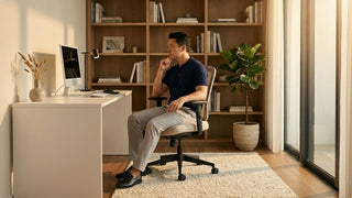 Man sitting on a small office chair in a warm modern home office with bookshelves