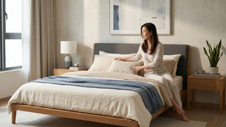 Woman arranging pillows on a wood bed frame in a calm small Singapore bedroom with neutral bedding and bedside tables.