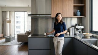 Woman standing beside a stainless steel kitchen cabinet in an open-plan Singapore home with wood upper cabinets and a bright living area.