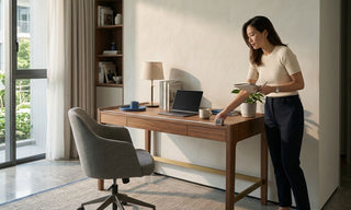 Woman measuring a wooden study desk in a bright 2-bedroom condo workspace with chair, laptop, and shelving.