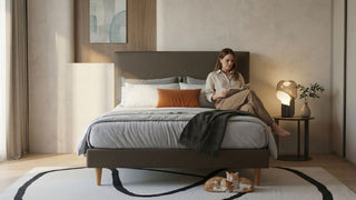 Woman reading on an upholstered bed in a warm Singapore bedroom with bedside lamp and cats under the bed