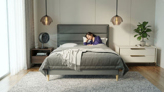 Woman sleeping beside a table fan in a cosy Singapore bedroom with grey bed and neutral decor