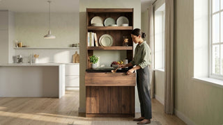 Woman using a tall wooden kitchen cabinet beside a bright kitchen window