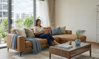 Tan faux leather L-shaped sofa in a bright Singapore apartment living room with coffee table and balcony plants.
