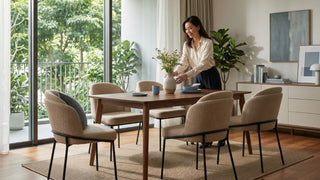 Woman styling a wooden dining table with beige upholstered dining chairs in a bright Singapore condo dining room.