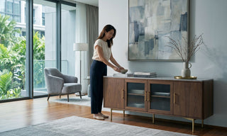 Woman styling a walnut sideboard with glass doors in a modern Singapore condo dining area.
