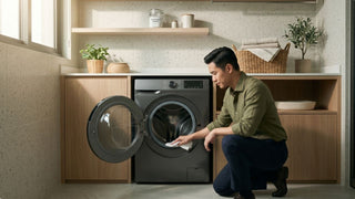 Man wiping the rubber seal of a front-load washing machine in a modern laundry room with cabinets and cleaning supplies
