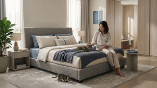 Woman sitting on a water-repellent upholstered bed frame with two cats in a bright Singapore bedroom.