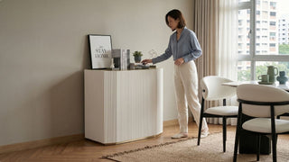 Woman styling a white buffet table beside a modern dining set in a Singapore home