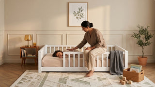 Mother sitting beside a sleeping child in a white toddler bed frame in a calm bedroom