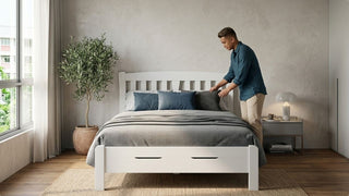Man arranging pillows on a white twin bed with under-bed storage in a modern Singapore bedroom