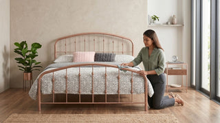 Woman wiping a rose gold metal bed frame in a modern bedroom as part of simple rust prevention and care