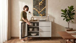 Woman arranging tableware inside a white sideboard table with glass door storage in a cosy Singapore dining room