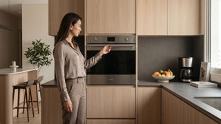 Woman checking a built-in steam oven in a modern kitchen with light wood cabinets and appliances