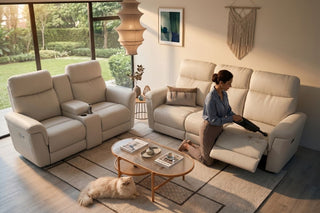 Woman cleaning a recliner sofa with a handheld vacuum in a warm modern living room with a cat