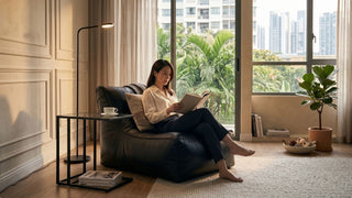Woman reading on a black lazy sofa chair near a balcony window, styled with a side table, coffee cup and indoor plant