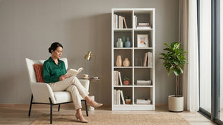 Woman reading beside a white bookshelf with books and decor in a warm studio apartment