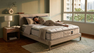 Woman resting on a luxury mattress in a cosy Singapore bedroom with warm green wall, bedside table, and large window