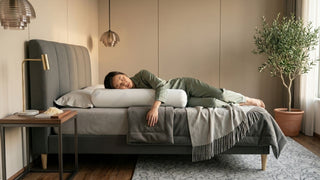 Woman sleeping with a white bolster pillow on a grey bed in a warm bedroom