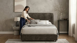Woman styling pillows on a grey queen bed frame in a modern Singapore condo bedroom