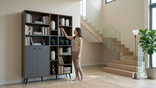 Woman reaching for books on a tall bookshelf beside a staircase in a bright Singapore maisonette