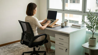 Woman using a wooden laptop stand on a white desk in a bright Singapore study corner
