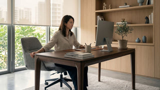 Woman working at a wooden desktop table in a bright Singapore home office with built-in shelves and natural light.
