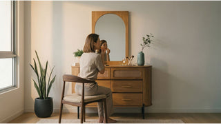Woman using a wooden dressing table with arched mirror near natural window light in a Singapore bedroom