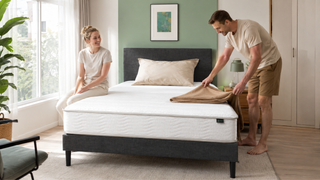 Zinus-style mattress on a charcoal fabric bed frame in a bright modern Singapore bedroom with a couple arranging bedding.